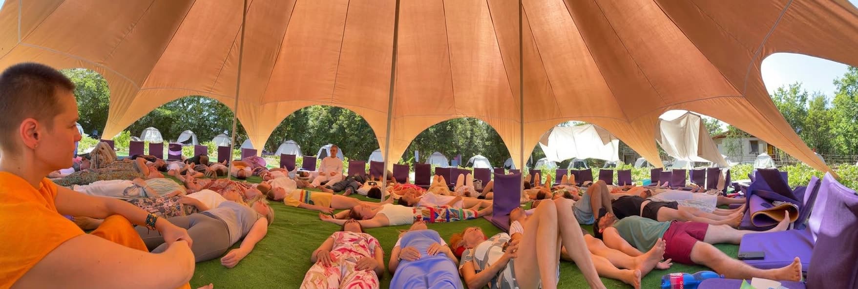 Participants lying in a wide circle for a group breathwork session under an open-sided tent