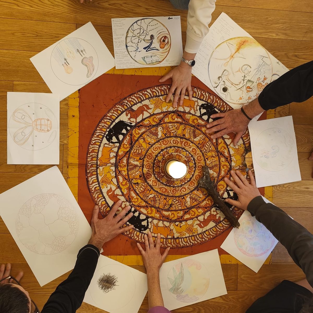 Hands gathered around a candle at the centre of a mandala